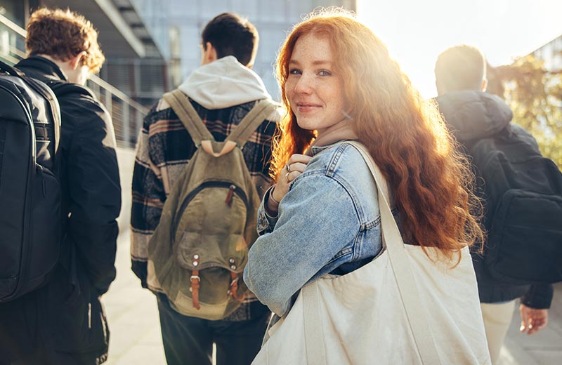 Girl with backpack looking at camera while walking.