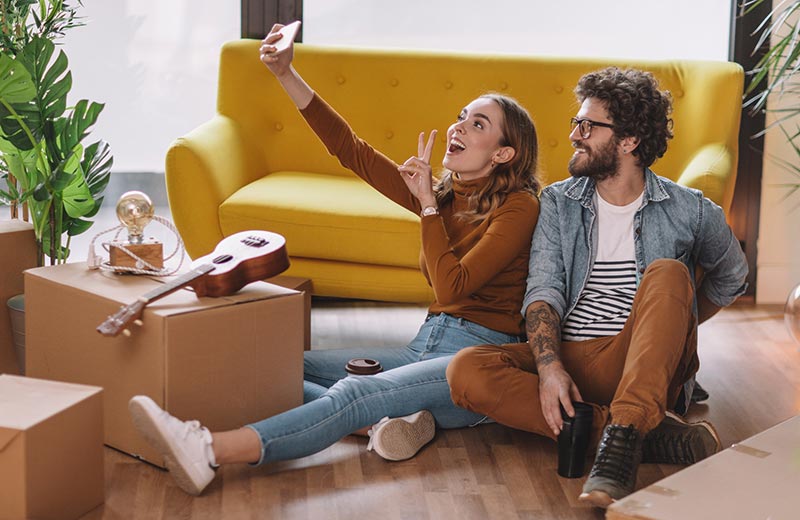 Gen Z couple taking selfie while unpacking boxes in new home.